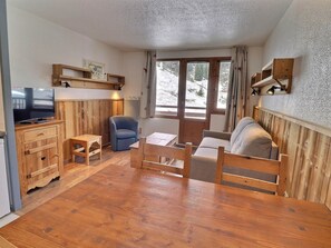 A cozy room with a wooden floor, a television, a sofa, a chair, and a table. - Comfortable 2 Rooms, Ski-in/Ski-out, 4 Pers. Near Shops (La Tania)