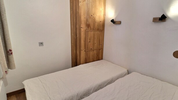 Een kleine kamer met twee bedden, houten lambrisering aan een muur en een lamp aan de overkant.
