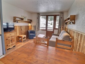 A cozy room with a wooden floor, a television, a sofa, a chair, and a table. - Comfortable 2 Rooms, Ski-in/Ski-out, 4 Pers. Near Shops (La Tania)