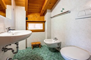 A bathroom with a sink, bidet, toilet, wooden step, and a window.