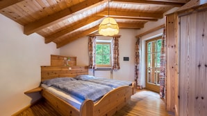 Una cama de madera en una habitación con techo inclinado, una ventana con cortinas y una puerta.