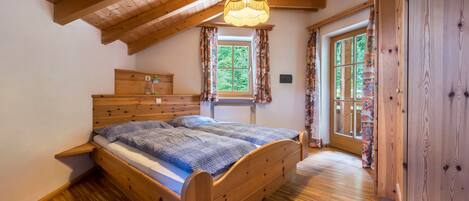 Una cama de madera en una habitación con techo inclinado, una ventana con cortinas y una puerta.