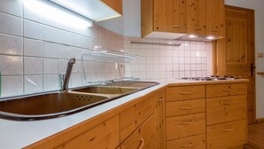 Una cocina con armarios de madera, un lavamanos de acero inoxidable y salpicadero de azulejos.