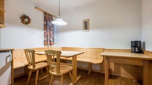 Una mesa de comedor de madera con sillas, un banco, una lámpara colgante, una cafetera y un refrigerador.