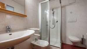 Un baño con lavamanos, bidé, inodoro y ducha con mampara de vidrio.