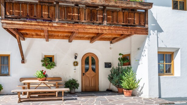 Un chalet traditionnel doté d’un balcon en bois, d’un sol en pierre et de plantes en pot.