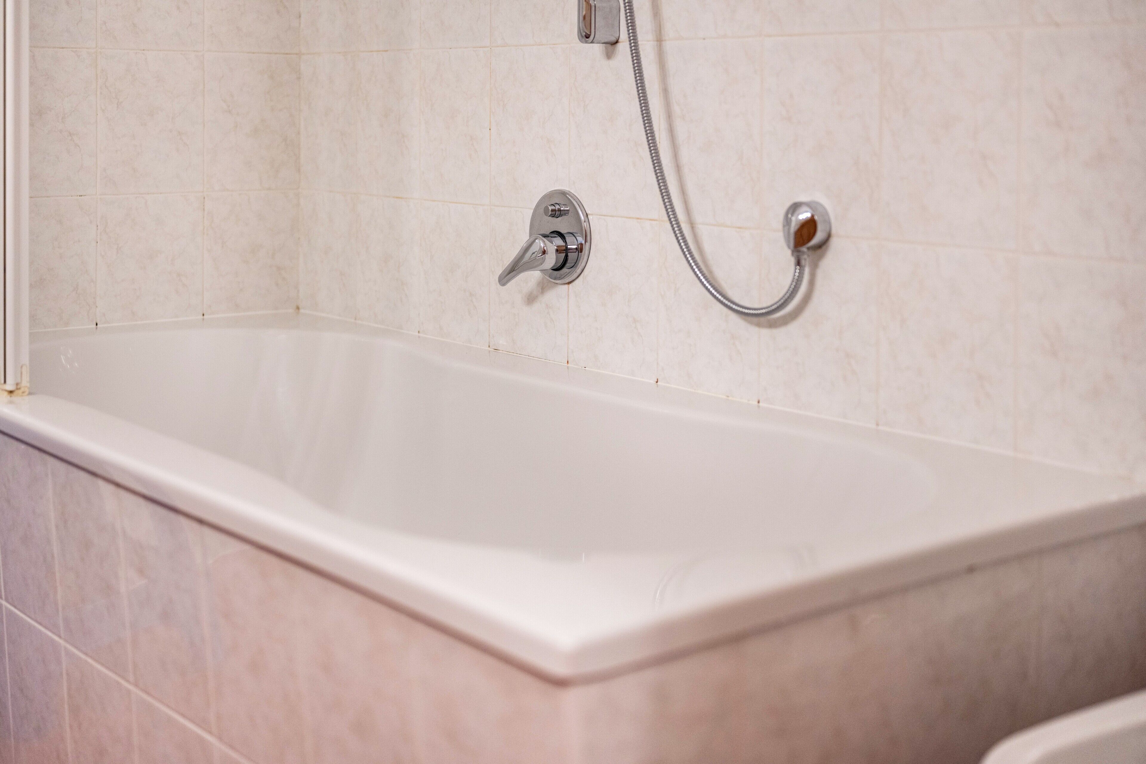 Eine Badewanne mit Duschkopf und Duschschlauch, geflieste Wände und ein Eckdesign.