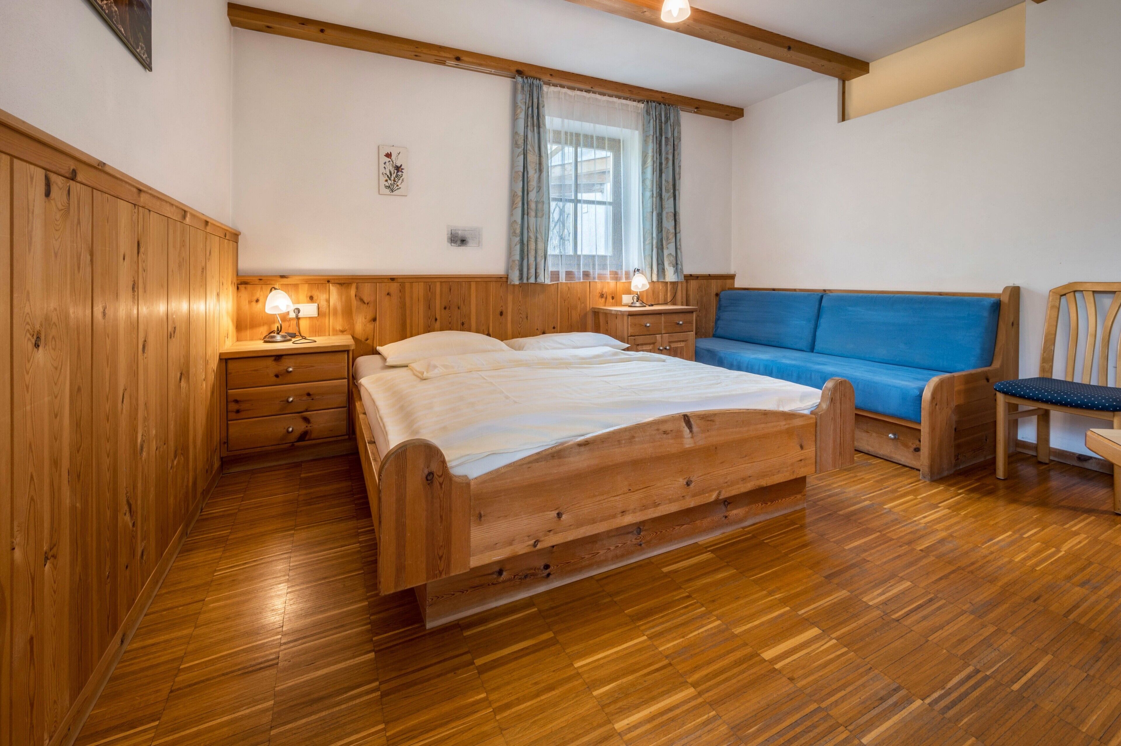 A wooden bedroom with a bed, bedside tables, a blue sofa, and a chair.