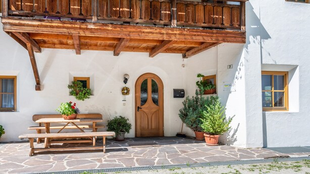 Un edificio tradicional con balcón de madera, entrada empedrada y plantas en macetas.
