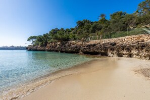 Une plage à l’eau claire, une falaise rocheuse et des arbres.