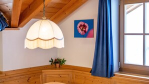 A wooden room with a bed, a hanging light fixture, a window with blue curtains, and a wall-mounted flower painting.