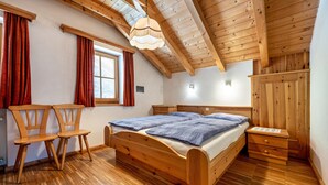A wooden bedroom with a bed, two chairs, a nightstand, and a wardrobe.