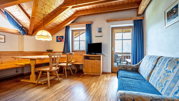 A cozy room with a wooden dining table, chairs, a sofa, a TV, and a window with curtains.