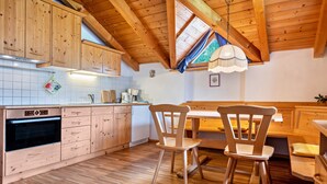 A wooden kitchen with a built-in oven, wooden cabinets, and a dining area with a bench and chairs.