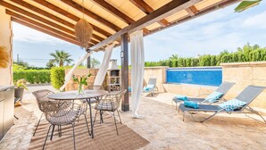En udendørs terrasse med et bord, stole, en pool og liggestole.