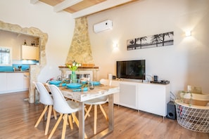 A modern kitchen with a stone arch, a dining area with white chairs, a TV, and a stone wall.
