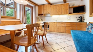 A kitchen with wooden cabinets, a dining table with chairs, a blue sofa, and a TV mounted above the counter.