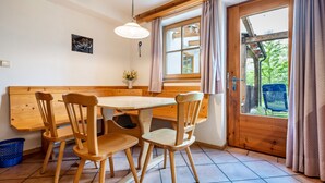 A wooden dining table with chairs, a vase with flowers, a window with curtains, and a door leading outside.