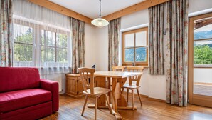 A room with a red sofa, wooden dining table, chairs, and curtains. - Holiday Apartment "Lindenhof 9" with Shared Garden & Wi-Fi (Vandoies)