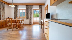 A room with wooden flooring, a dining area with chairs, a kitchen with a refrigerator, and large windows with curtains. - Holiday Apartment "Lindenhof 9" with Shared Garden & Wi-Fi (Vandoies)