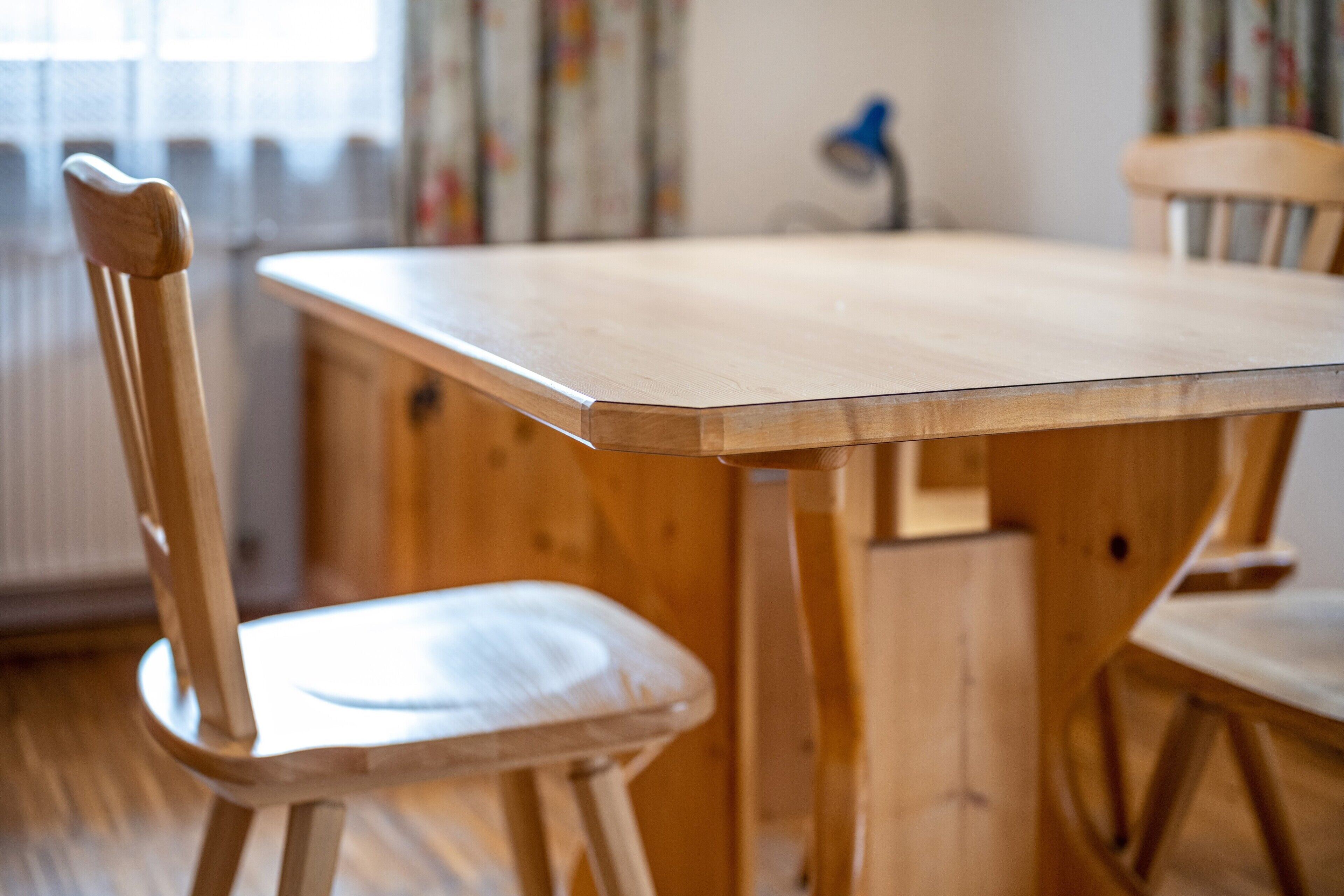 Een houten eettafel met stoelen, een radiator en een lamp op de achtergrond.