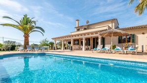 A poolside area with lounge chairs, a palm tree, and a building with a tiled roof and windows. - Holiday Home 'Villa Sun Club Home' with Private Pool, Wi-Fi and Air Conditioning (Llucmajor)