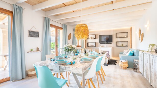 A dining area with a wooden table set for six, surrounded by chairs, a hanging light fixture, and a kitchen in the background. - Holiday Home 'Villa Sun Club Home' with Private Pool, Wi-Fi and Air Conditioning (Llucmajor)