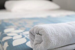 Une serviette blanche, soigneusement pliée, est posée sur un lit recouvert d’une couvre-lit à motifs floraux bleus.