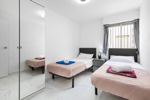 Une chambre d’hôtel avec une porte en verre, deux lits avec une literie rose, une table de chevet et une fenêtre avec des rideaux.