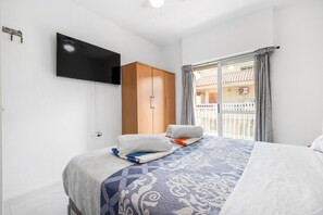 Een hotelkamer met een bed, een kledingkast, een televisie en een balkon met gordijnen.