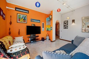 A living room with a flat-screen TV, orange walls, and a sofa with patterned cushions.