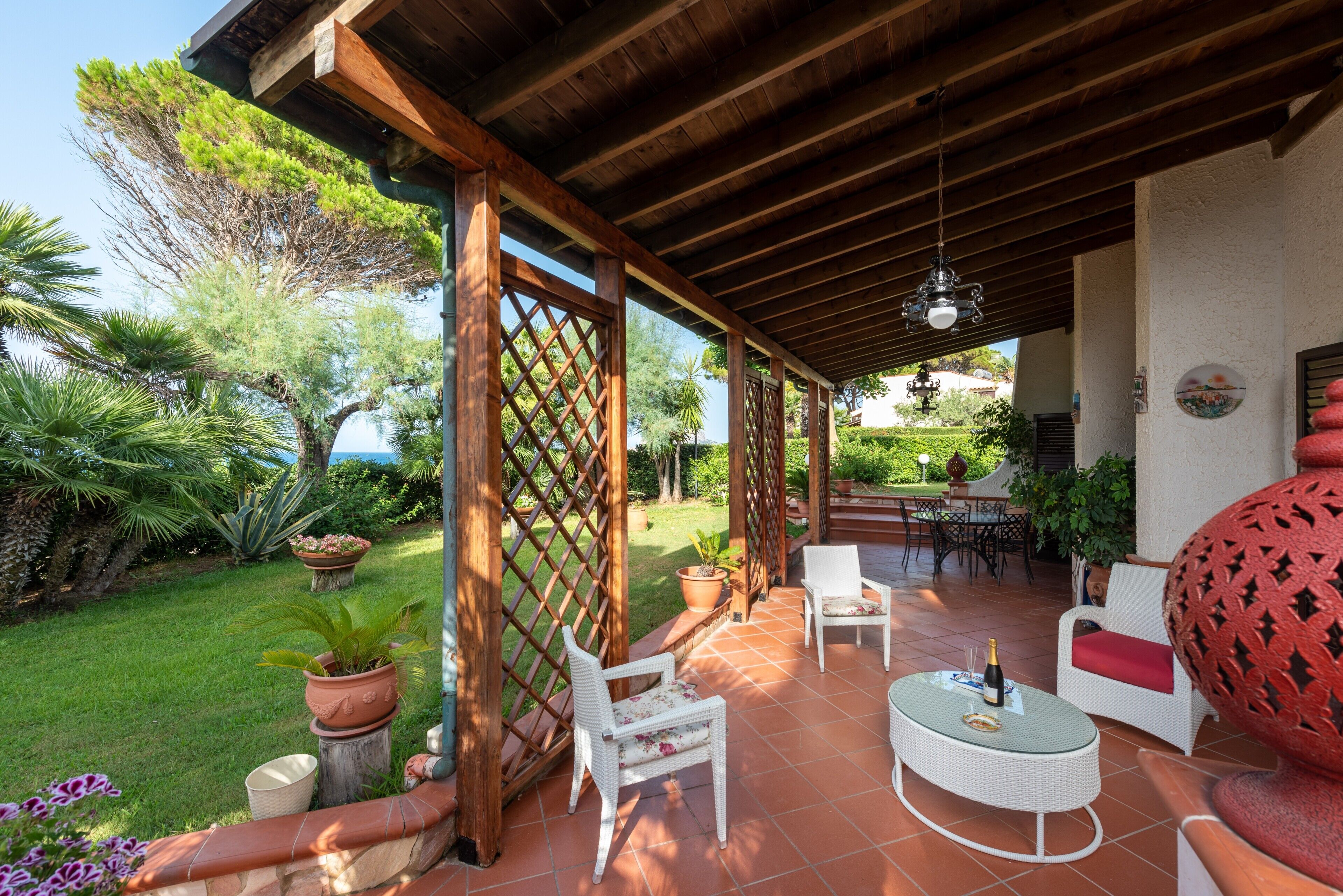 Une terrasse extérieure avec des poutres en bois, des meubles en osier blanc et des plantes en pot.