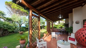 Eine Terrasse im Freien mit Holzbalken, weißen Korbmöbeln und Topfpflanzen.