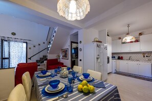 A dining area with a table set for four, a kitchen in the background, and a staircase leading to another level.