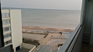 Une vue depuis une fenêtre donnant sur une plage, avec un ciel dégagé.