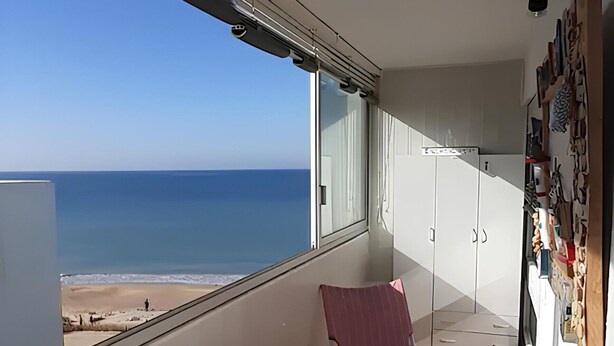 Un balcon avec vue sur la mer, une table recouverte d’une nappe à motifs géométriques et un mur orné de divers objets.