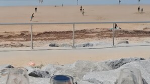 Une plage avec des personnes à l’arrière-plan, une rambarde et des rochers au premier plan.