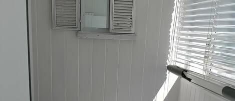 A small, single-bed room with a tiled floor, a window with blinds, and a radiator.
