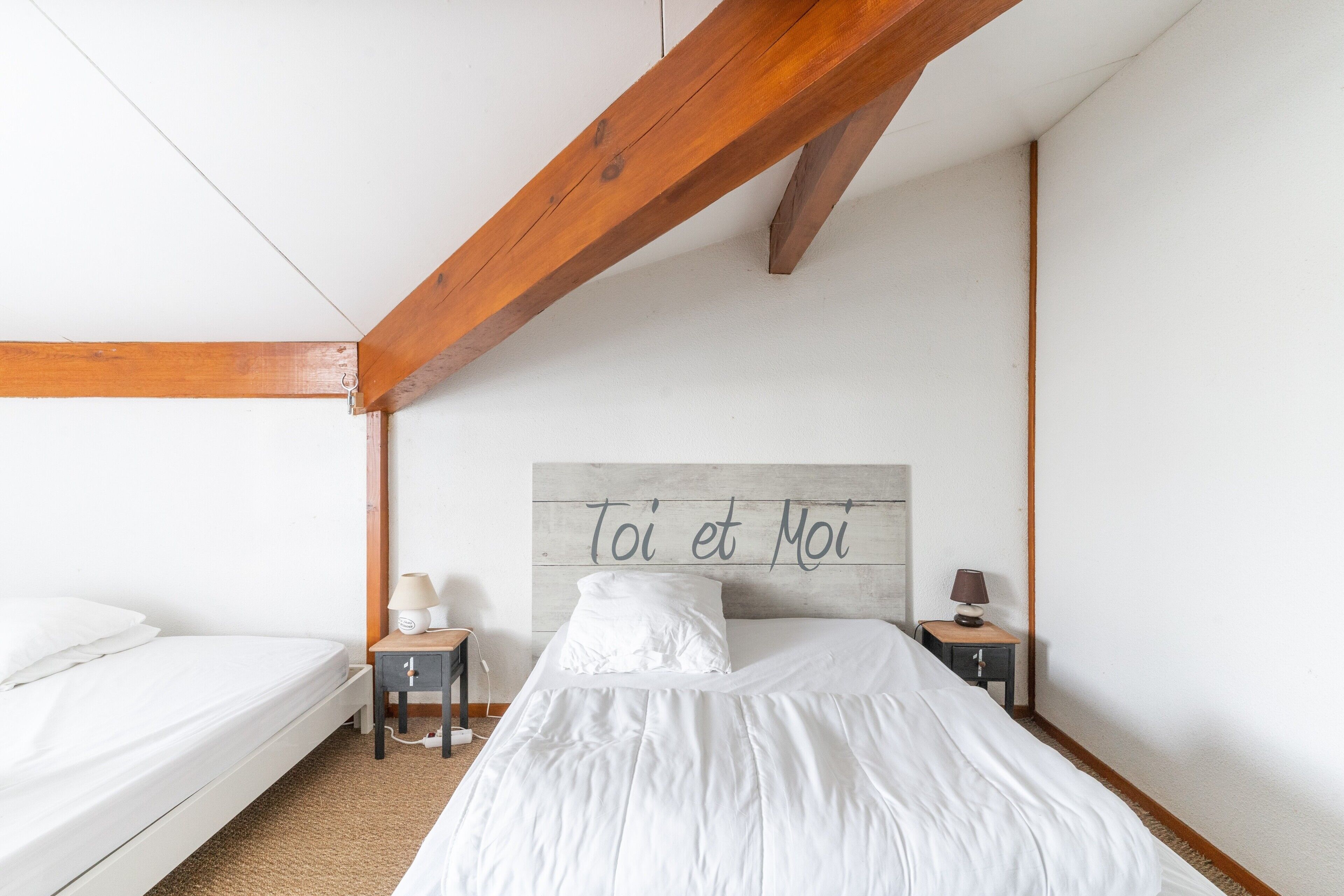 Ein Schlafzimmer mit Bett, Nachttischen, einem Kopfende mit Text und freiliegenden Holzbalken.