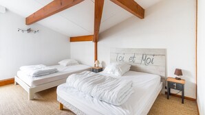 Ein Schlafzimmer mit zwei Betten, Holzbalken, einer Deckenleuchte, einem Nachttisch mit Lampe und einer Wand mit der Aufschrift 'toi et moi'.