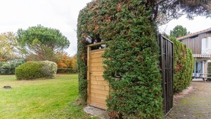 Eine Holztür, teilweise von Efeu überwuchert, ein gepflasterter Weg und ein Gebäude mit einem Ziegeldach im Hintergrund.