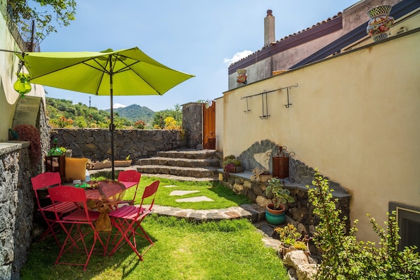 Une terrasse avec une table et des chaises, un parasol vert et des plantes en pot.