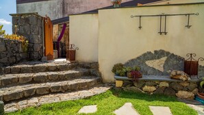 A stone staircase leading to a door with a purple curtain, a stone wall with a decorative arch, and a small garden area with potted plants. - Holiday Home "Sikelia Relais" with Mountain View & Wi-Fi (Linguaglossa)