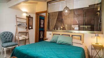 Un dormitorio con cama, una silla, estante, espejo y ventana con cortinas.