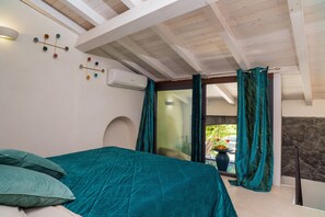 Une chambre à coucher avec un lit, des rideaux de couleur turquoise, une vue sur l’extérieur et un mur en pierre.