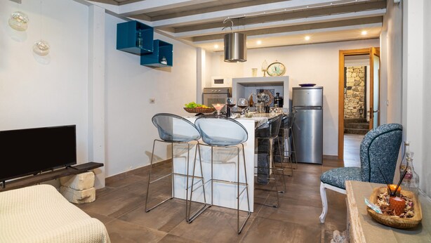 A modern kitchen with a dining area, bar stools, a TV, and a stone wall. - Holiday Home "Sikelia Relais" with Mountain View & Wi-Fi (Linguaglossa)