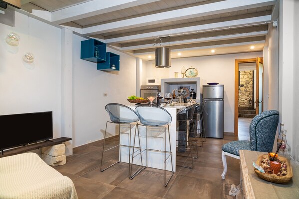 A modern kitchen with a dining area, bar stools, a TV, and a stone wall. - Holiday Home "Sikelia Relais" with Mountain View & Wi-Fi (Linguaglossa)