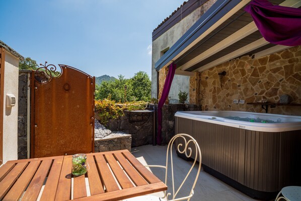 An outdoor patio with a wooden table, a hot tub, and a stone wall.