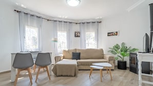 Een woonkamer met een bank, twee stoelen, een bijzettafeltje, een potplant, een open haard en een televisie.