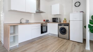 Een moderne keuken met witte kasten, een roestvrijstalen afzuigkap, een magnetron, een oven, een wasmachine en een koelkast.